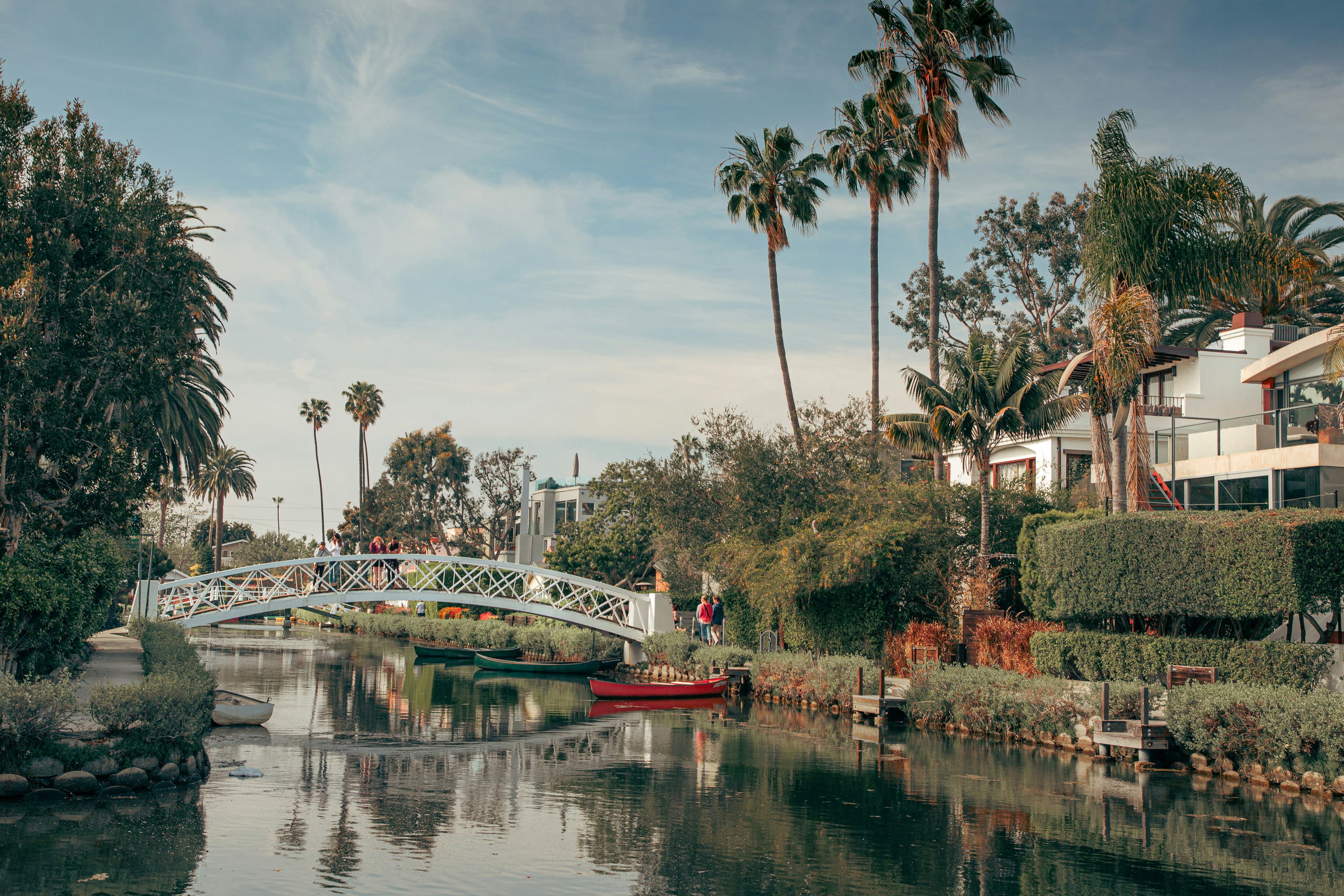 A white bridge over a canal with palm trees and houses